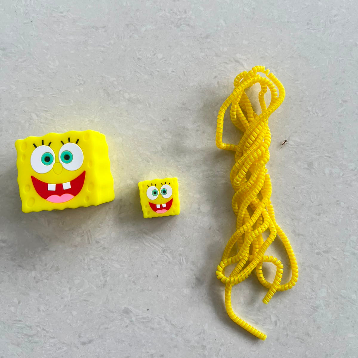 Yellow square smiley character charger adapter cover, mini cable protector and yellow spiral cable wrap components flat lay on grey surface
