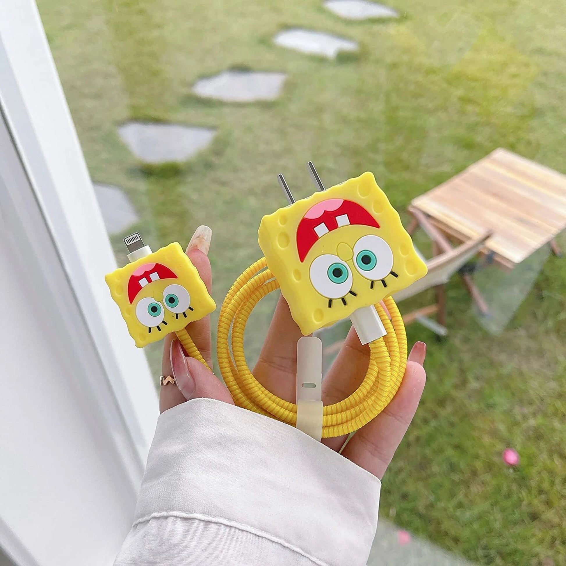 Yellow square smiley character charger cover and mini cable protector with yellow spiral cable wrap held in hand outdoors