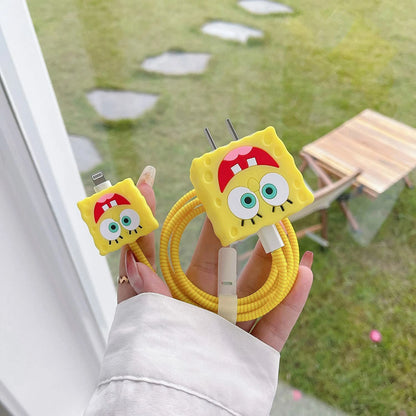 Yellow square smiley character charger cover and mini cable protector with yellow spiral cable wrap held in hand outdoors