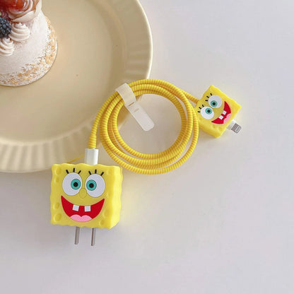 Yellow square smiley character charger cover and mini cable protector with yellow spiral cable wrap on white surface next to cake