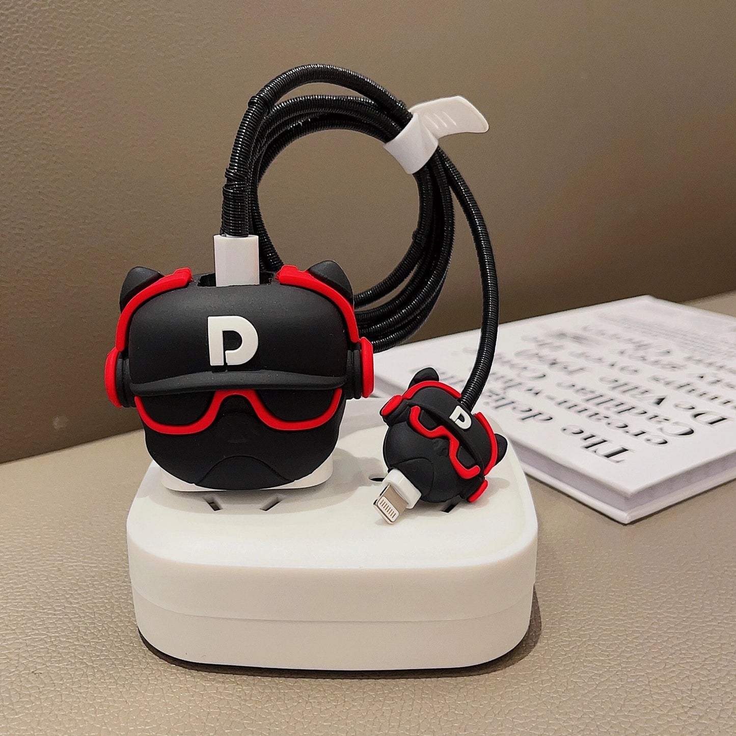 Black DJ character charger adapter cover on iPhone with mini cable protector on white surface