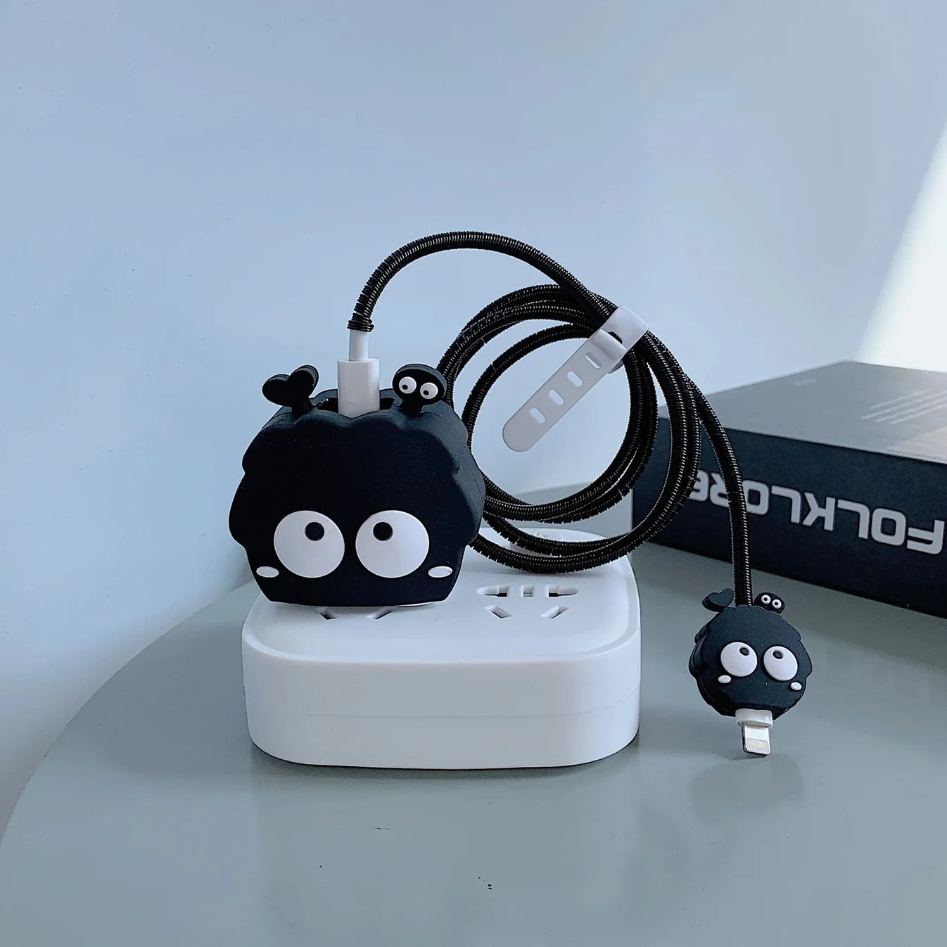 Black fluffy spirit charger cover and mini spirit cable protector with black spiral cable wrap flat lay on white surface