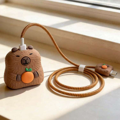 Capybara charger adapter cover on windowsill with golden coil winder and mini capybara cable bite - sunlit lifestyle shot