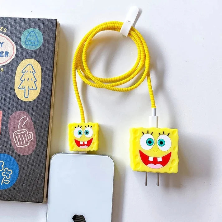 Yellow square smiley character charger cover and mini cable protector with yellow spiral cable wrap flat lay on white surface