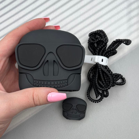 Matte black skull AirPods case with cable protector and lanyard on white fur background