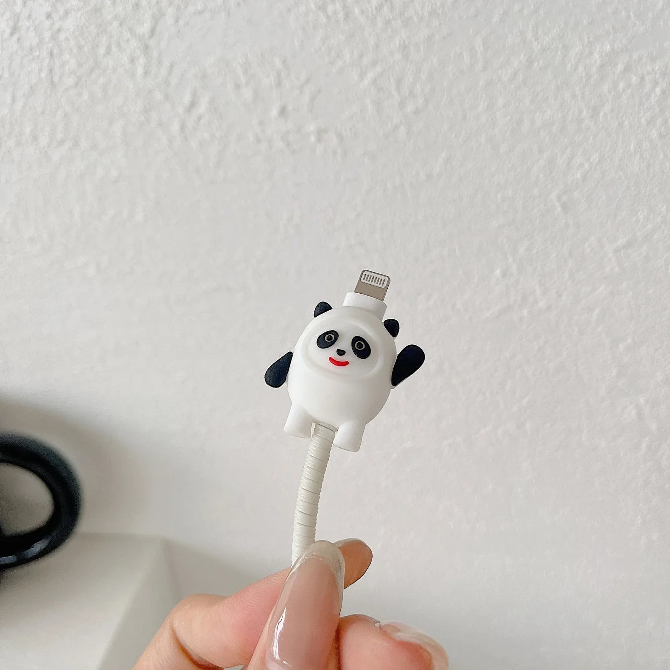 Panda face charger adapter cover lifestyle shot next to black ceramic mug on white shelf