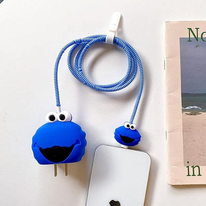 Blue fuzzy monster charger cover on adapter with blue spiral cable wrap on white surface next to book