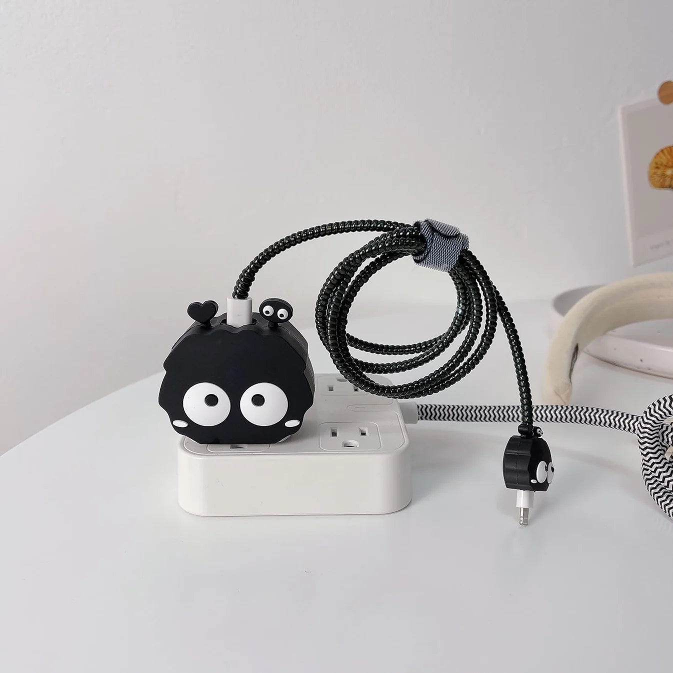 Black fluffy spirit charger cover plugged into power strip on white desk next to book