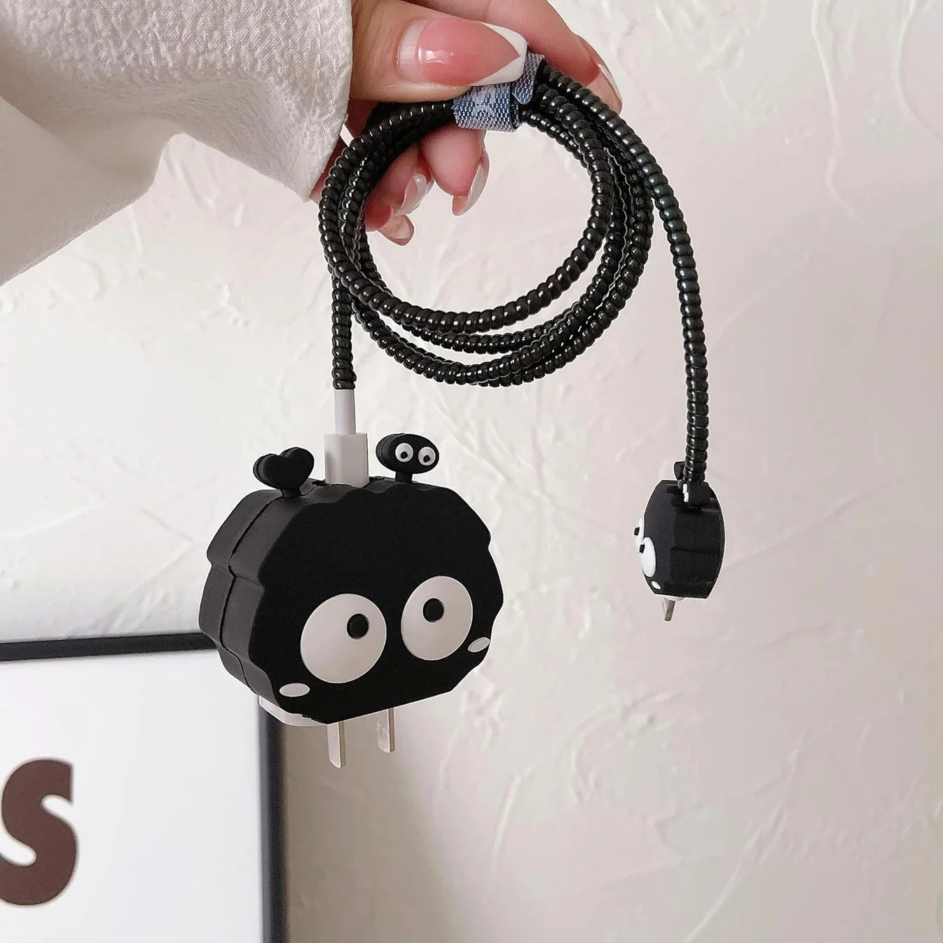 Black fluffy spirit charger adapter cover and mini spirit cable protector components flat lay on white surface