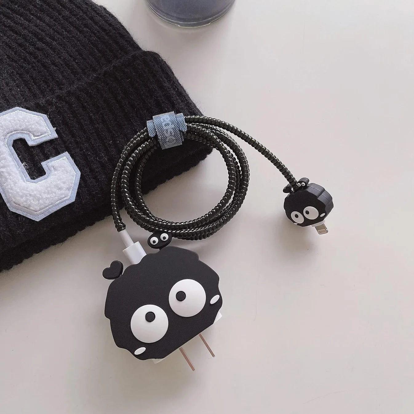 Black fluffy spirit charger cover and mini spirit cable protector with black spiral cable wrap on white surface next to black cap