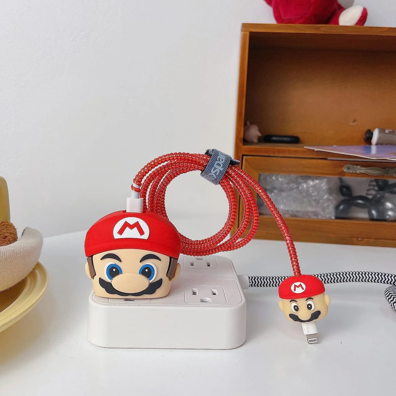 Red cartoon character charger cover and cable protector set held up near Christmas tree