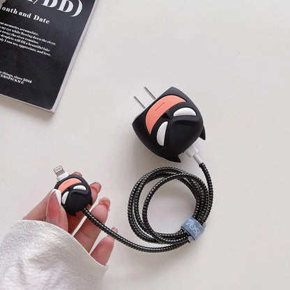 Dark masked hero charger adapter cover and mini cable protector with black spiral cable wrap flat lay on white surface next to magazine