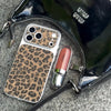 Black handbag with leopard print phone case and pink lipstick on a gray surface