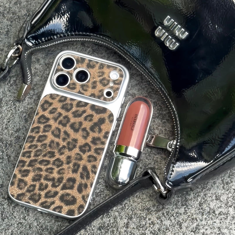 Black handbag with leopard print phone case and pink lipstick on a gray surface