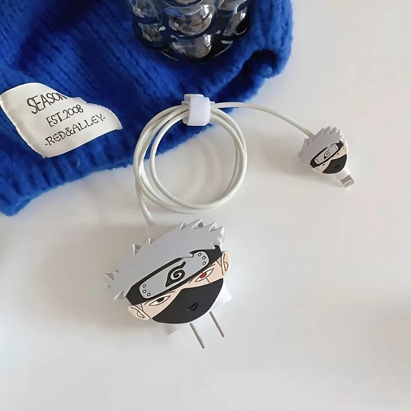 Grey masked ninja charger cover on adapter with white cable wrap next to blue knit hat on white surface