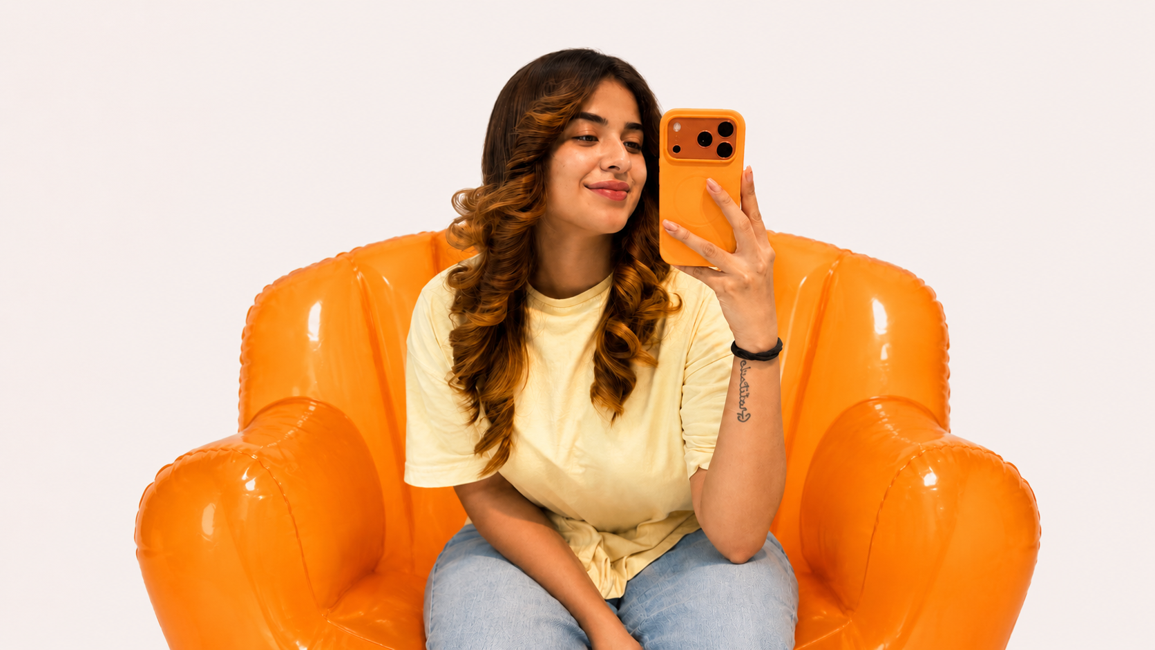 Woman taking a selfie on an orange inflatable chair against a white background
