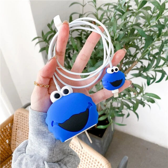 Blue fuzzy monster charger cover and mini monster cable protector held in hand with plant background