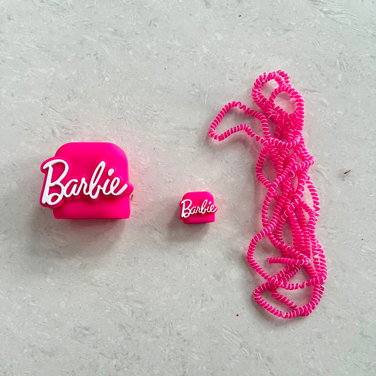 Hot pink silicone charger adapter cover, mini cable protector and spiral cable wrap components laid flat on white surface