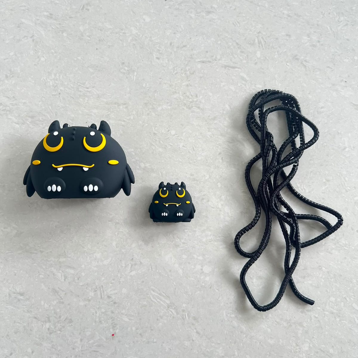 Dark monster charger adapter cover, mini monster cable protector and black spiral cable wrap flat lay on grey surface