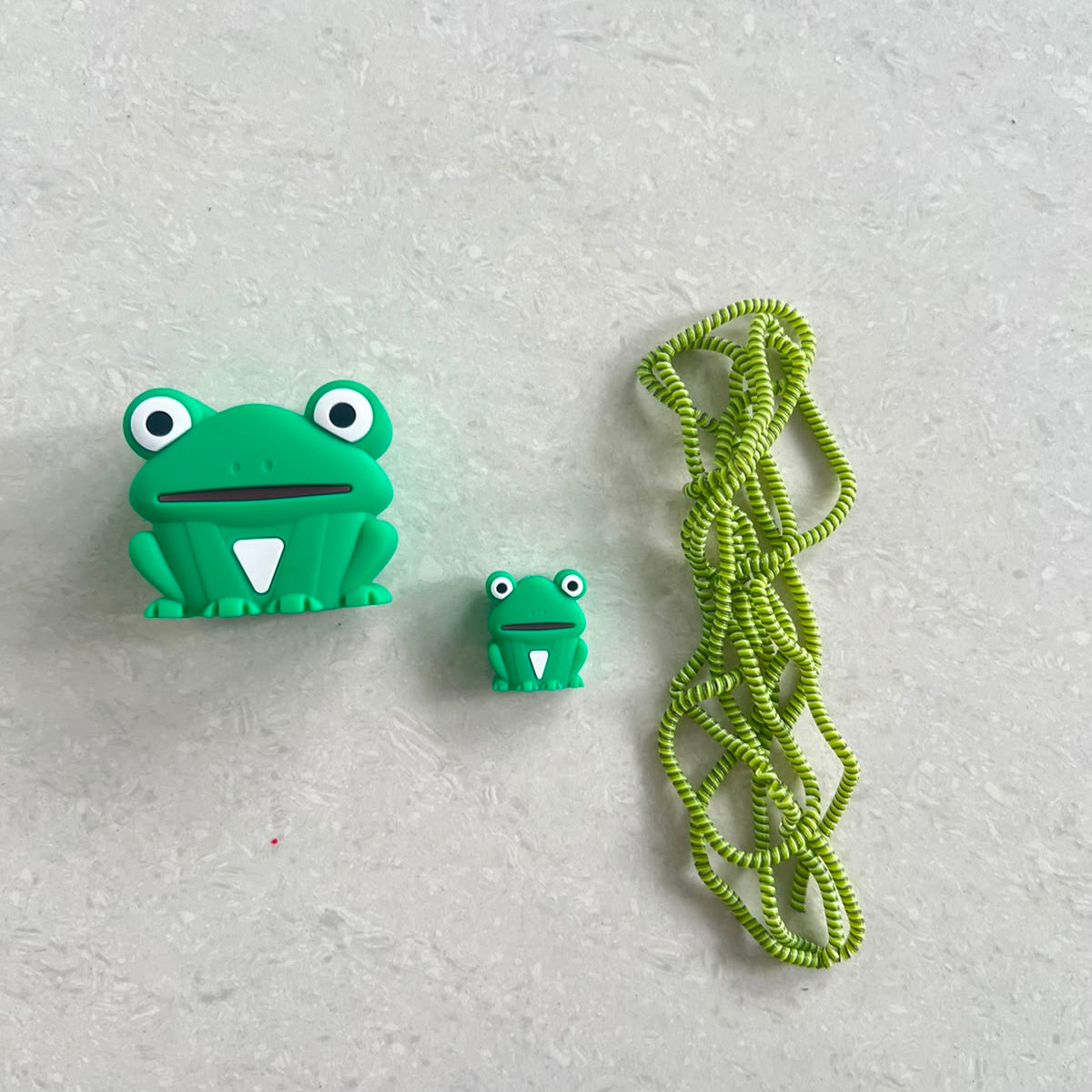 Green frog charger adapter cover, mini frog cable protector and green spiral cable wrap flat lay on white surface