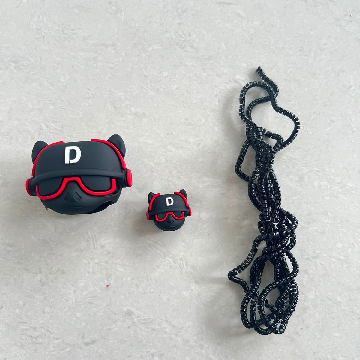 Black DJ character charger adapter cover, mini cable protector and black spiral cable wrap components flat lay on grey surface