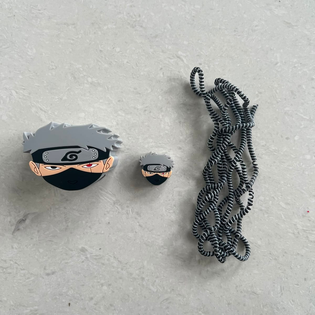 Grey masked ninja charger adapter cover, mini ninja cable protector and black white spiral cable wrap flat lay on grey surface
