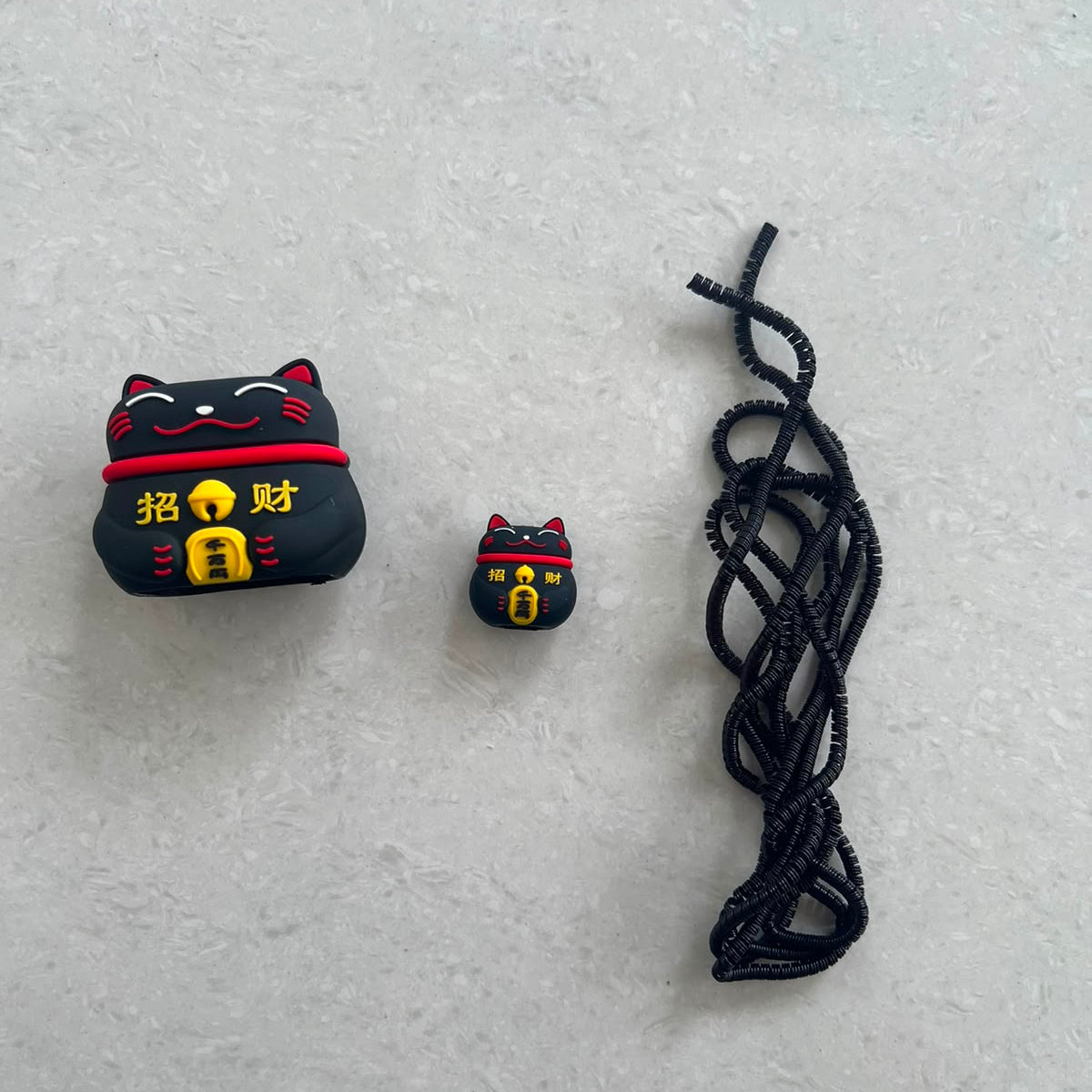Black fortune cat charger adapter cover, mini fortune cat cable protector and black spiral cable wrap flat lay on grey surface