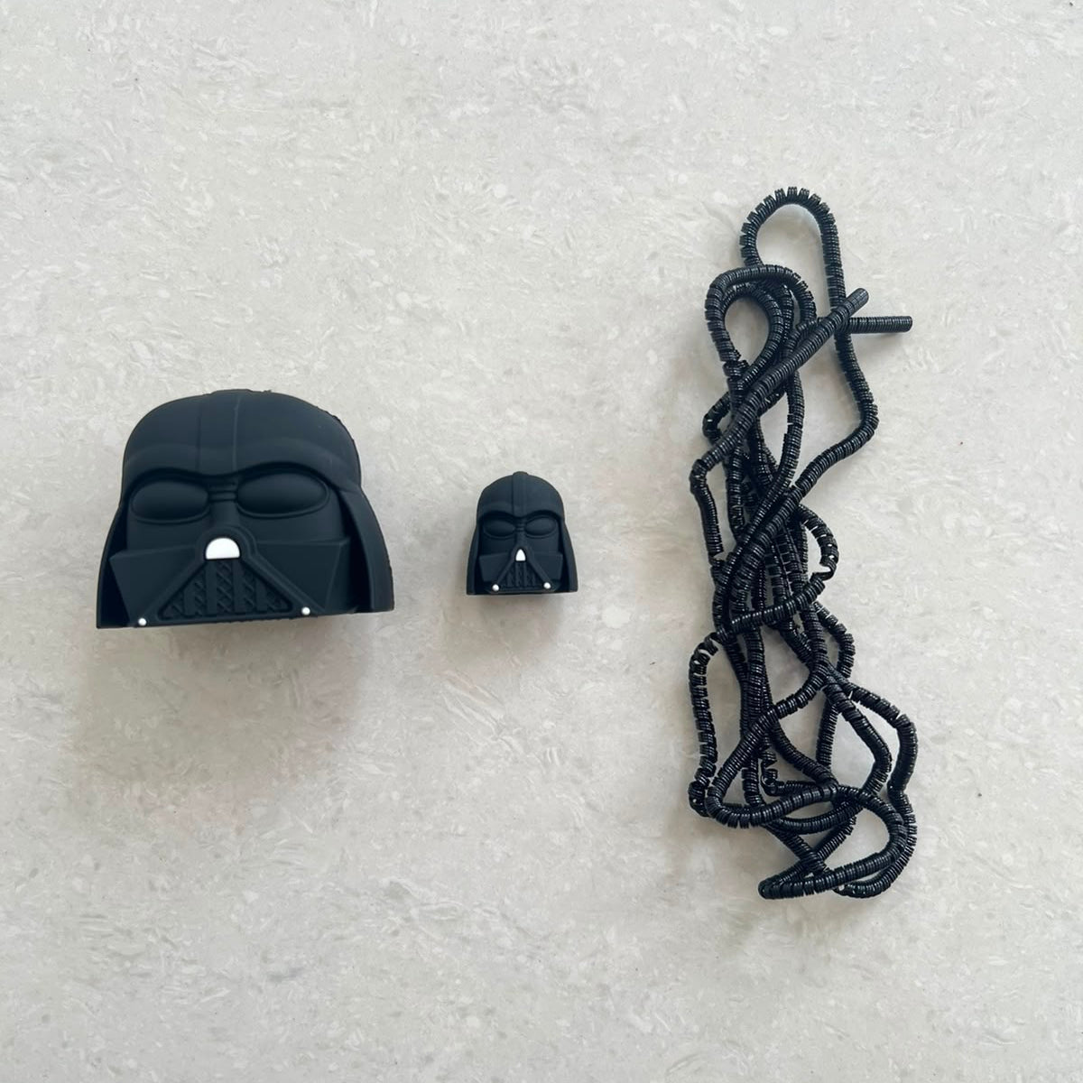 Matte black dark space villain helmet charger cover, mini helmet cable protector and black spiral cable wrap flat lay on grey surface