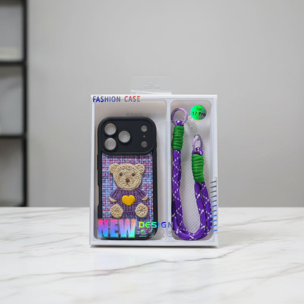 A phone case in its retail packaging, featuring a purple and pink knitted-texture teddy bear design with a yellow heart, alongside a matching purple and green woven wrist strap.
