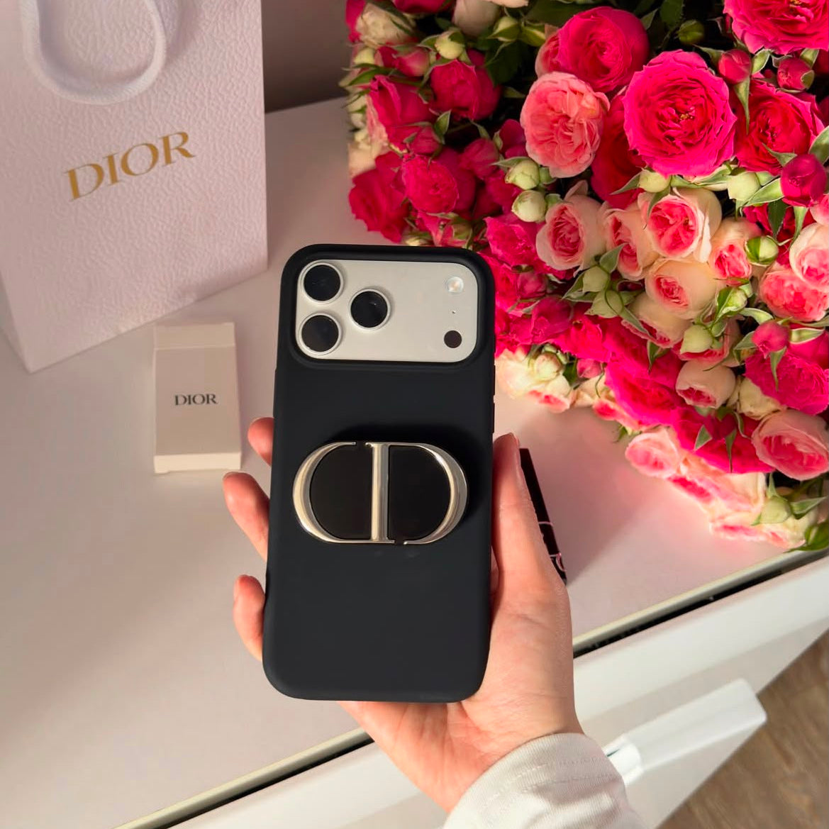 Monogram phone grip attached to black iPhone case with roses in background