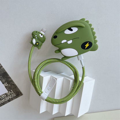 A green cartoon dinosaur-shaped charging cable holder and matching cable on a white display stand against a light gray wall.