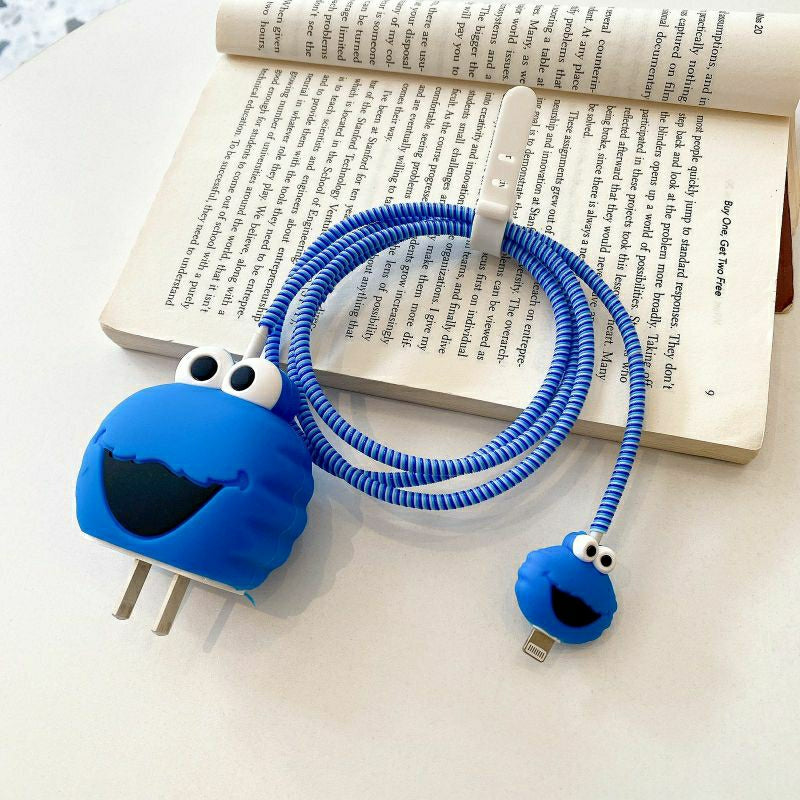 Blue fuzzy monster charger cover and mini monster cable protector with blue spiral cable wrap on white surface next to open book