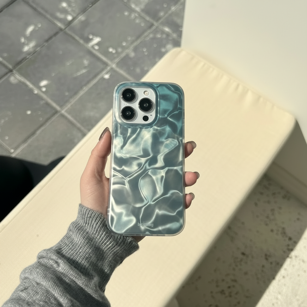 Hand in grey knit sweater holding ocean water ripple teal iPhone case outdoors in sunlight