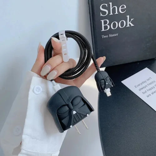 Matte black dark space villain helmet charger cover and mini helmet cable protector held in hand with black spiral cable wrap next to book